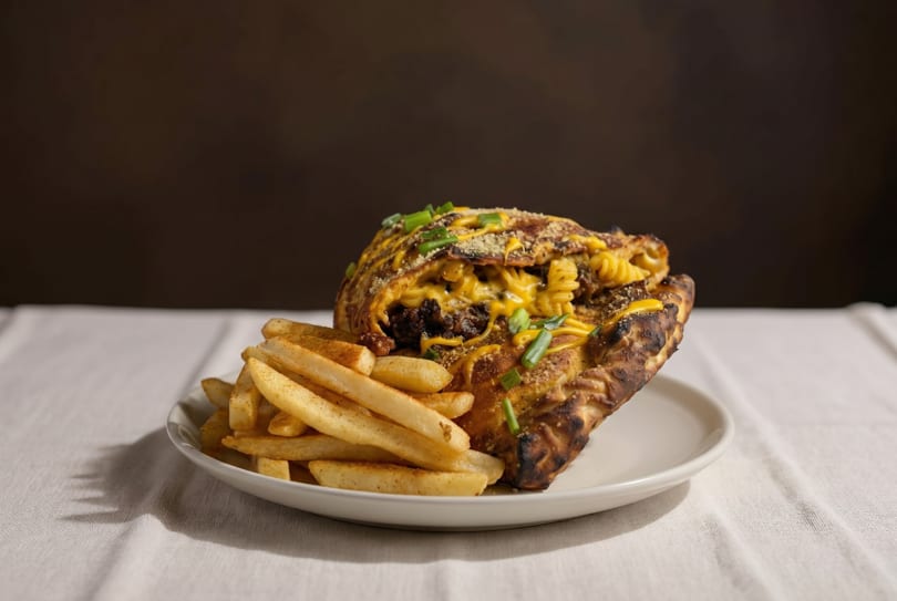 A calzone filled with macaroni and cheese, ground beef, and green onions, served with fries.