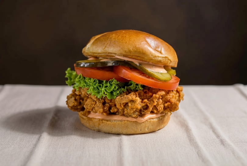 Crispy fried chicken sandwich with lettuce, tomato, pickles, and sauce on a bun.